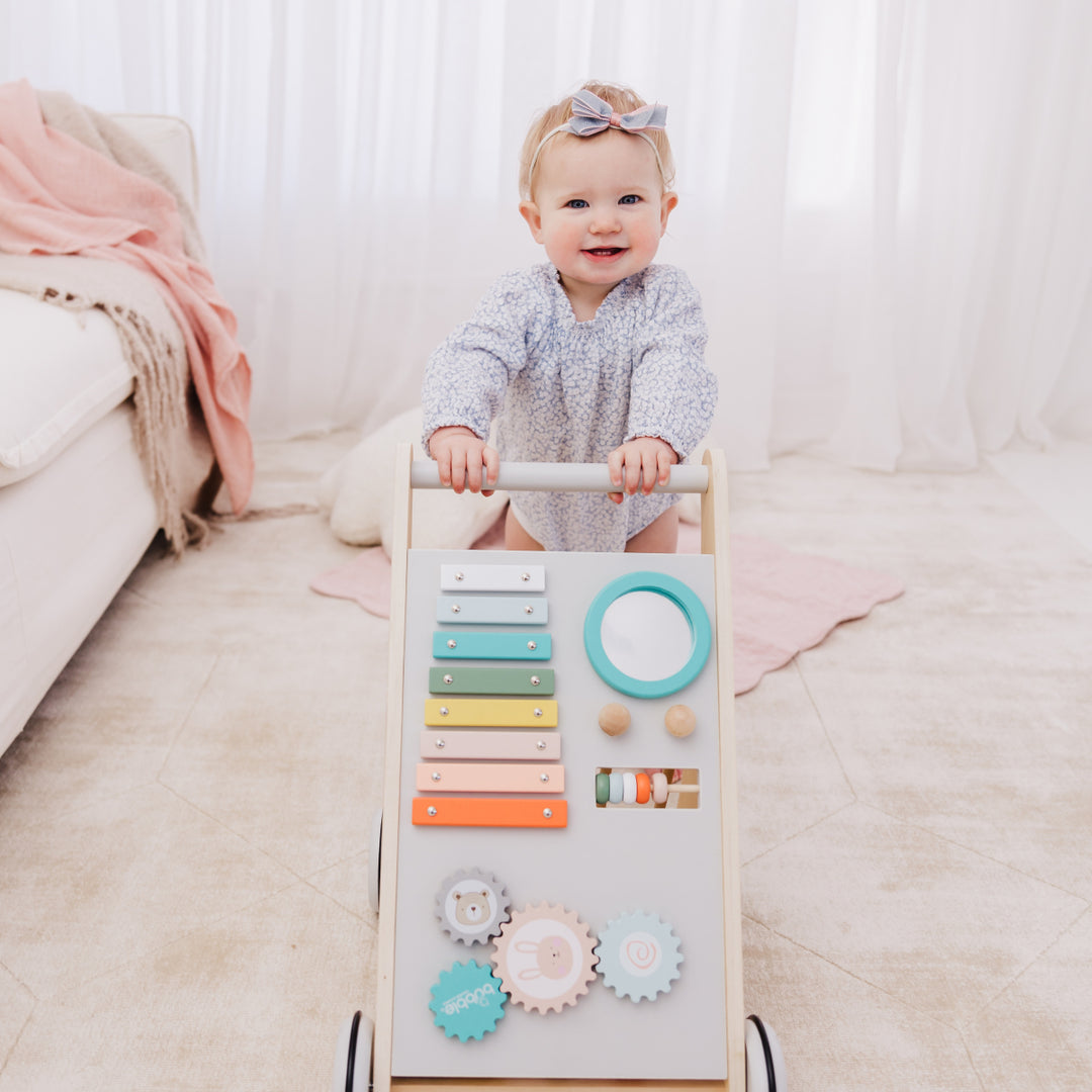 Baby playing with a colorful wooden activity board on a light-colored floor.