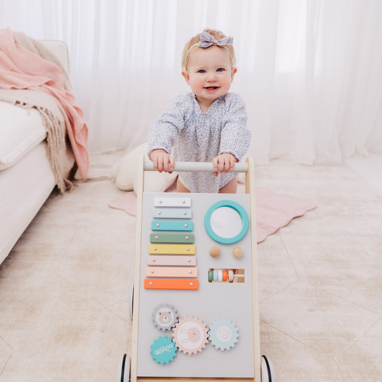 Baby playing with a colorful wooden activity board on a light-colored floor.