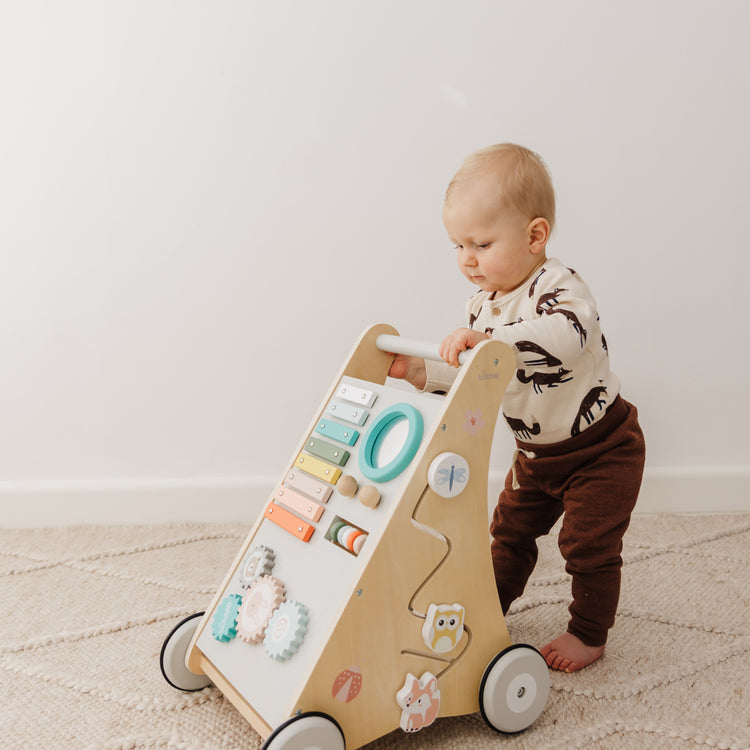 Baby playing with a wooden activity walker on a carpeted floor.