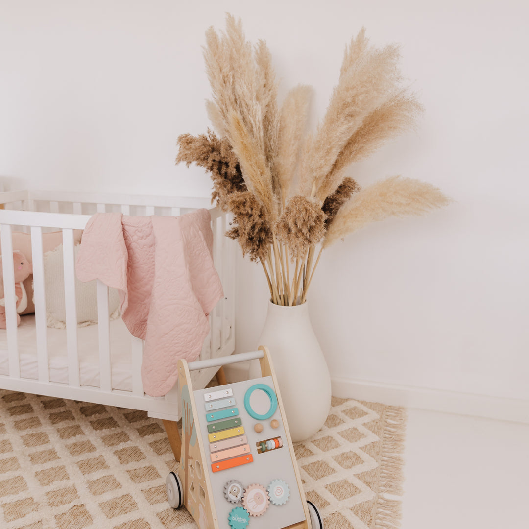 Nursery room with crib, decorative vase with pampas grass, and educational toy on a patterned rug.