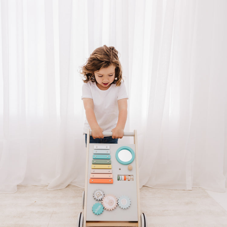 Child playing with a wooden toy ladder against a white curtain backdrop