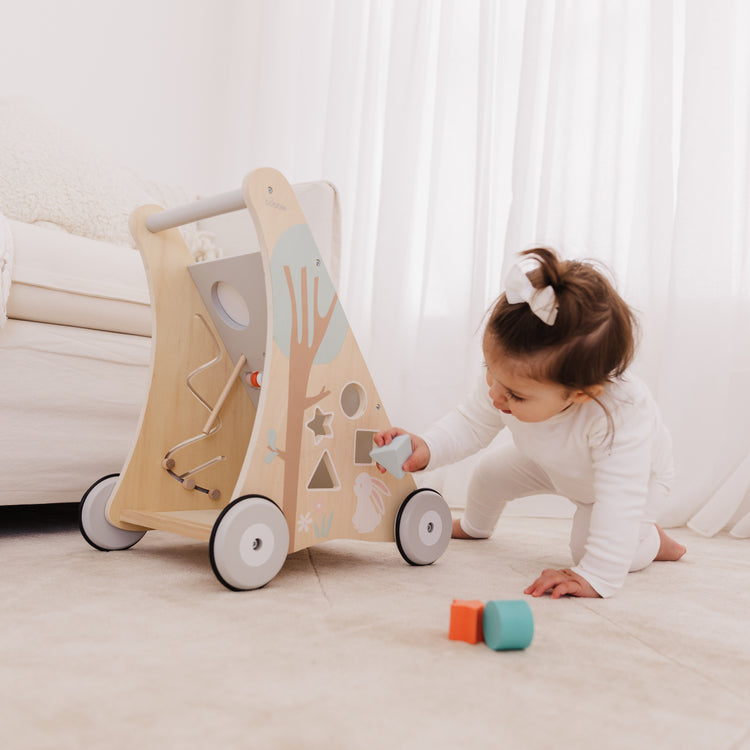 Child playing with a wooden toy walker on a light-colored floor.