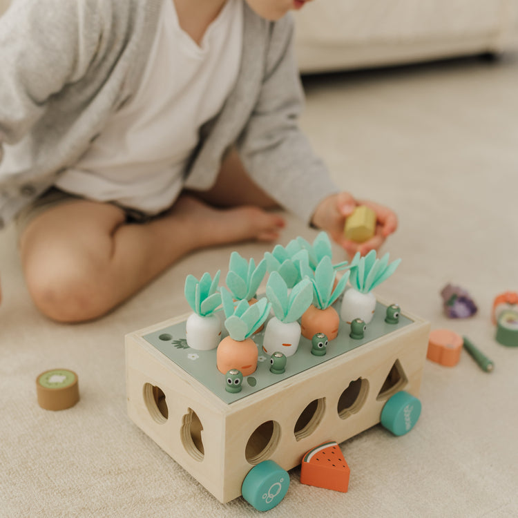 Child playing with a wooden toy featuring colorful shapes on a light-colored floor.
