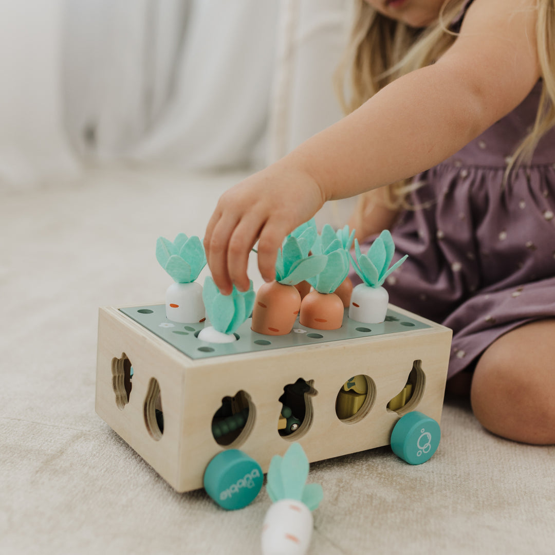 Child playing with a wooden toy that has colorful shapes and animals on a light surface.