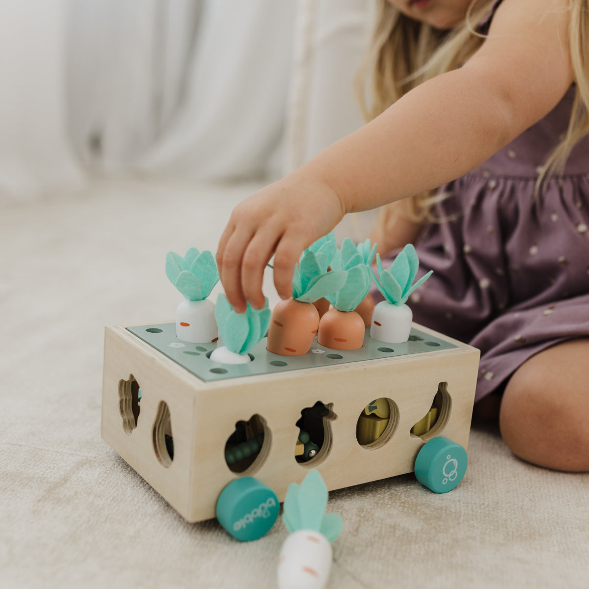 Child playing with a wooden toy that has colorful shapes and animals on a light surface.