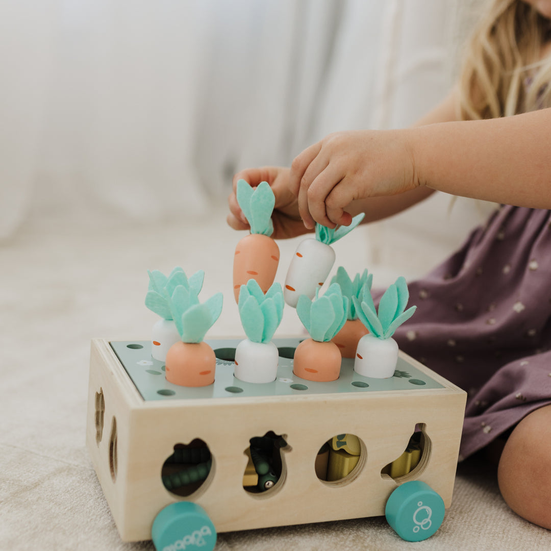 Child playing with a wooden toy featuring colorful plant-shaped pieces on a light surface.