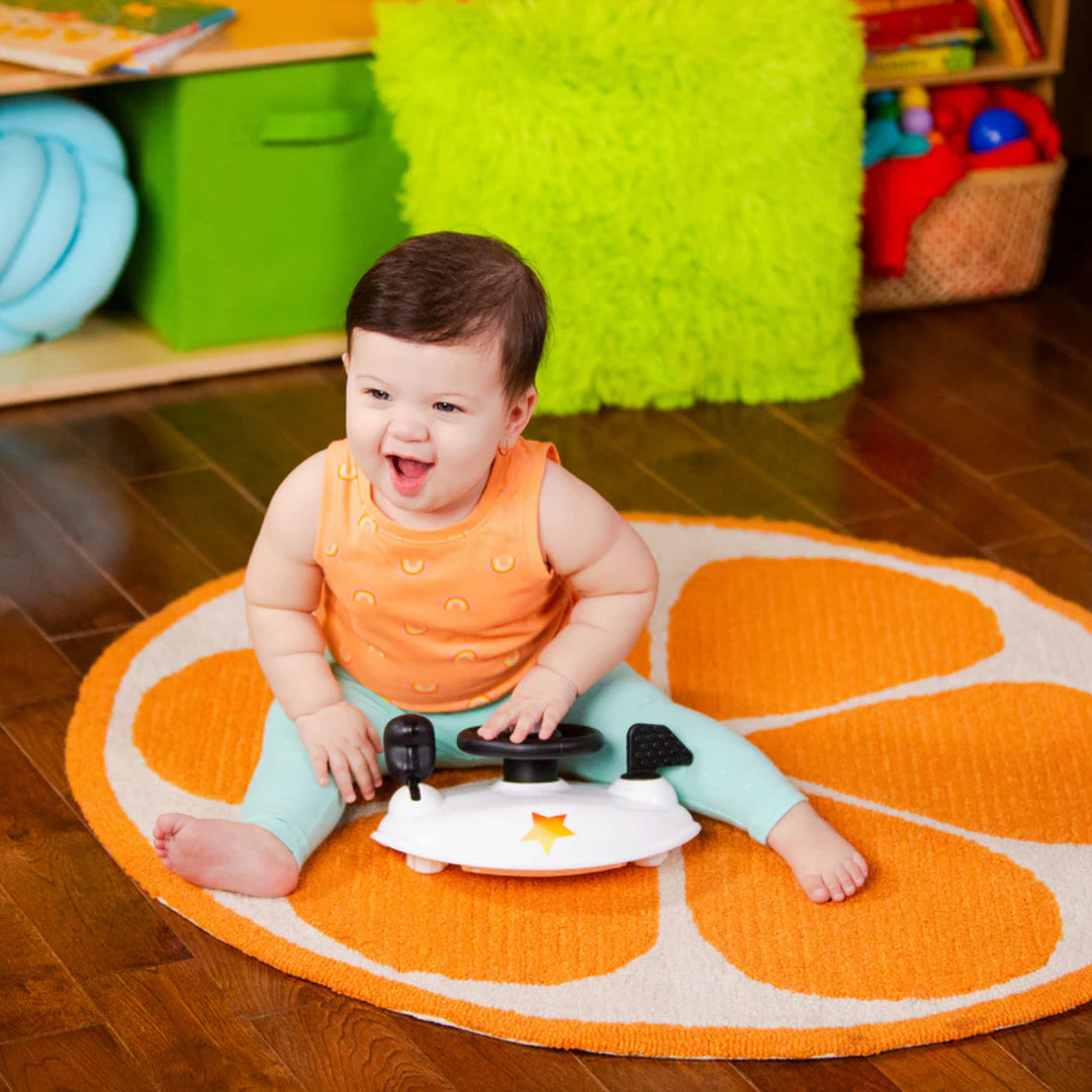 Baby playing with a toy car on an orange-shaped rug in a colorful room.