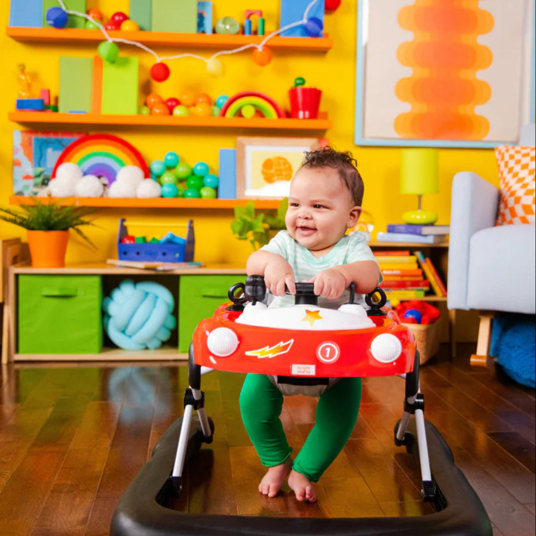 Child in a colorful room with toys and furniture, using a red toy car walker.