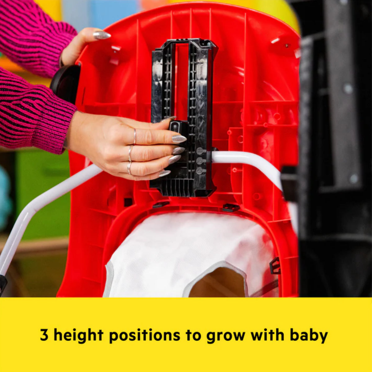 Red baby high chair with hands adjusting it, set against a blurred background.
