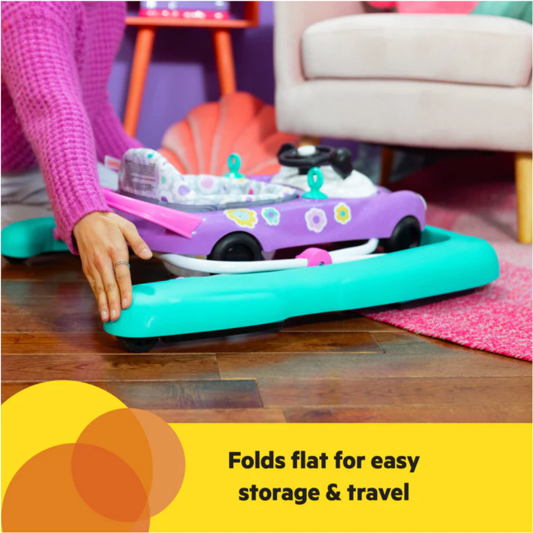Child's toy walker being folded flat on a wooden floor with text 'Folds flat for easy storage & travel'.