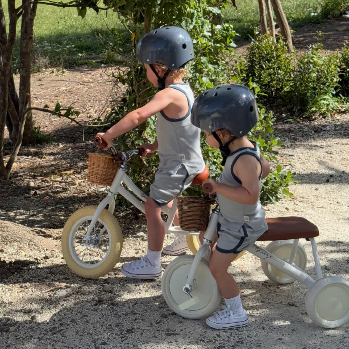 Two children riding balance bikes with training wheels in a natural setting.