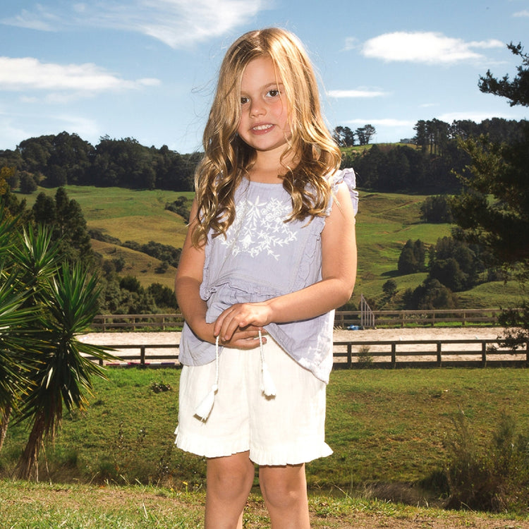 Young girl standing outdoors with a scenic background of green hills and trees.