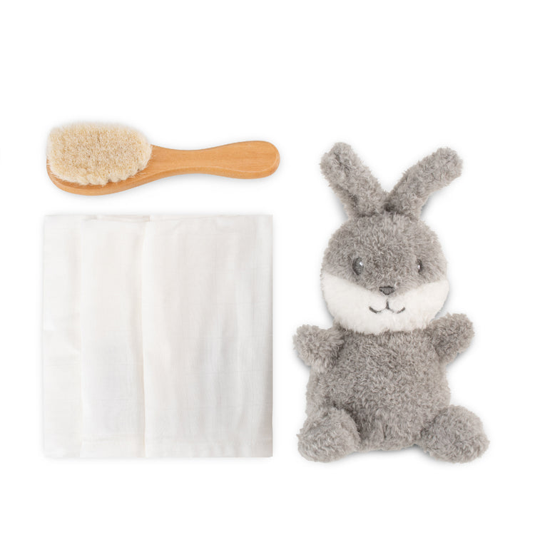 Gray plush bunny toy with a wooden brush and white towel on a white background