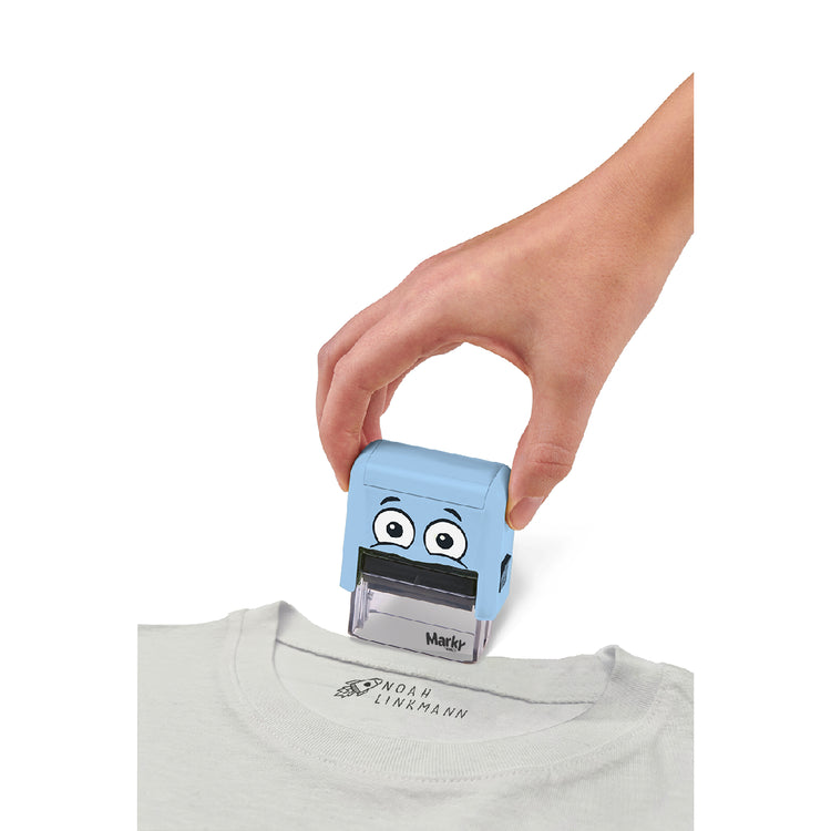 Hand using a blue cartoon character stamp on a white shirt with a visible brand logo.