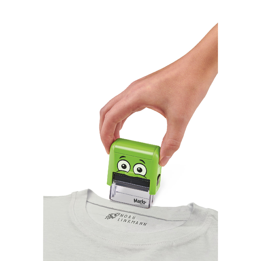 Green cartoon-style stamp being pressed onto a gray shirt with a visible brand logo.