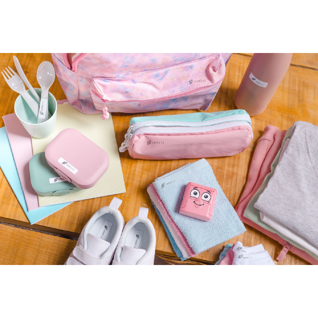 Collection of travel accessories including bags, pouches, and a pink pouch with a face on a wooden surface.