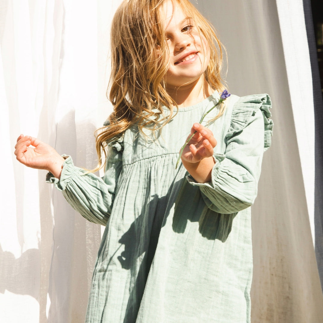 Young girl in a light green dress standing in front of sheer curtains