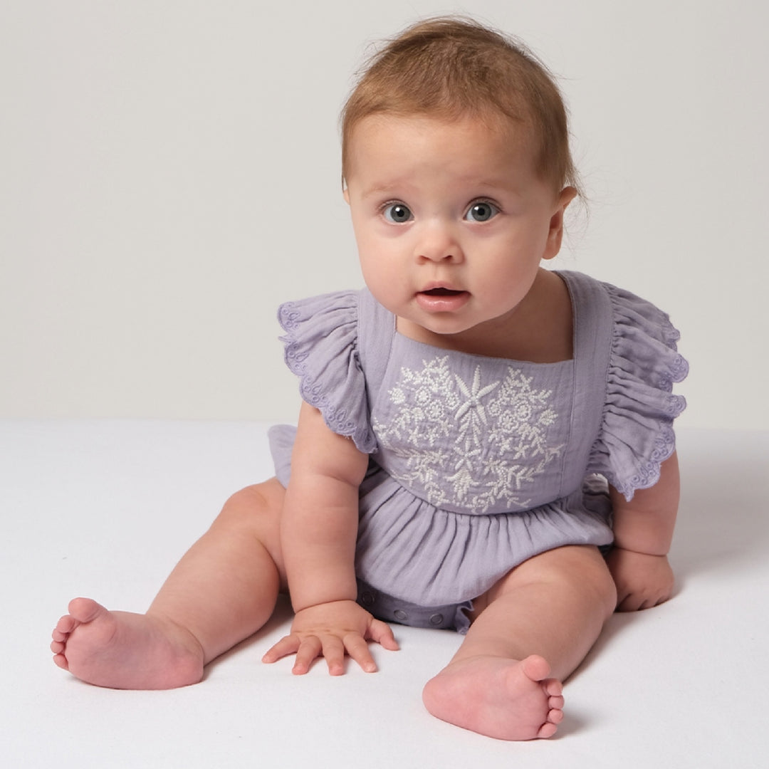 Baby wearing a light purple romper with ruffled sleeves on a white background