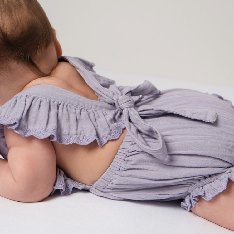 Baby wearing a light purple outfit with ruffled details on a white background
