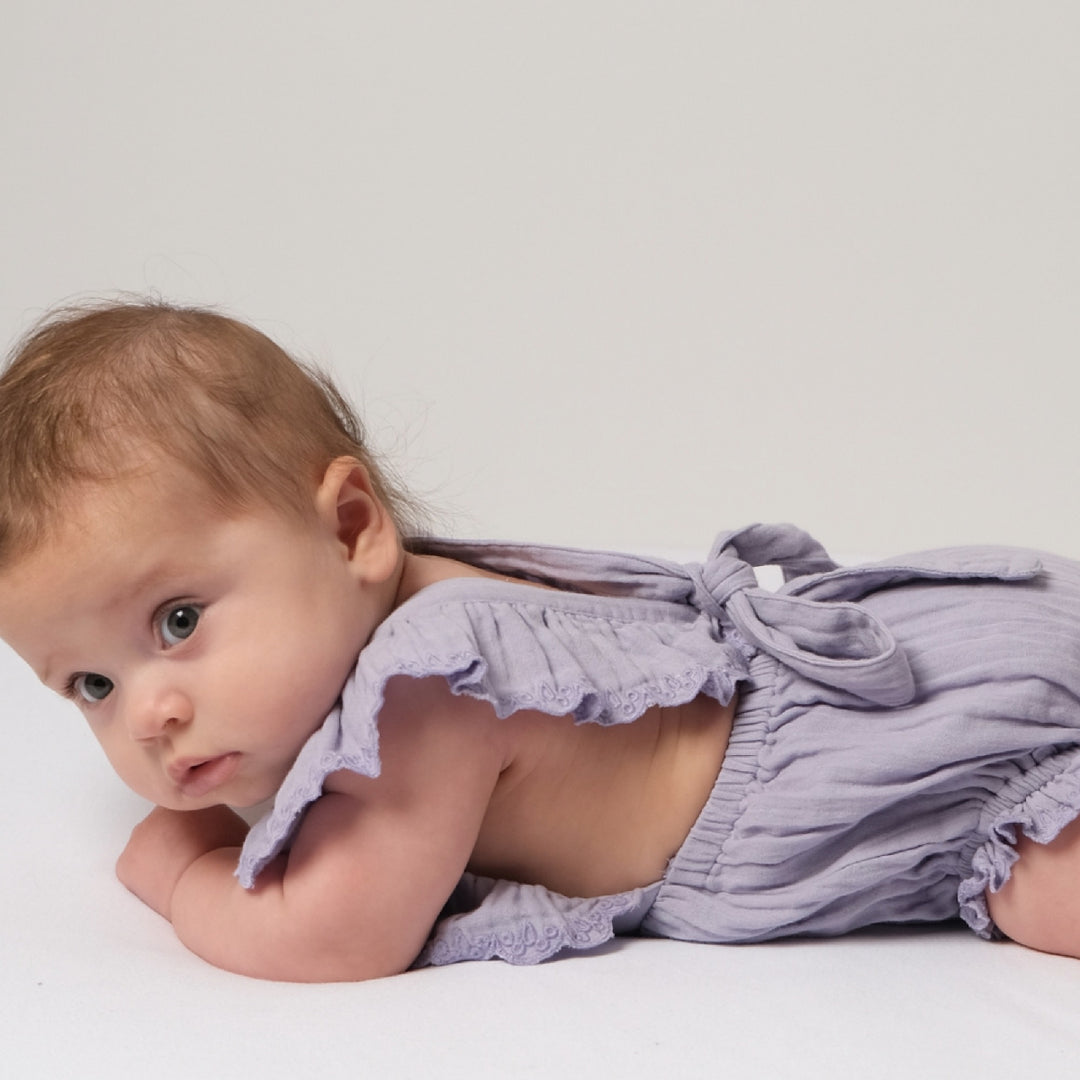 Baby wearing a light purple outfit lying on a white surface