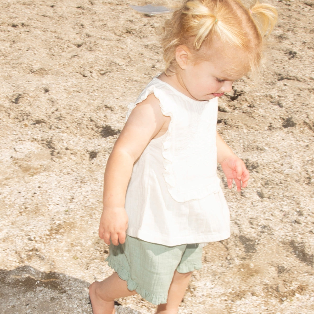 Young child in a white sleeveless top and light green shorts standing on a textured stone surface.