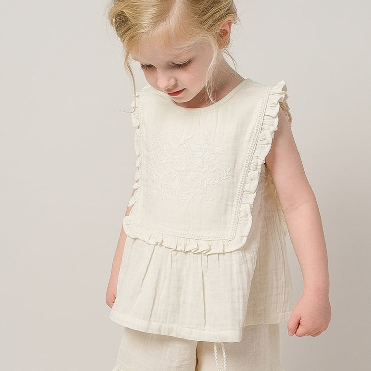 Young girl wearing a white ruffled top and pants against a plain background