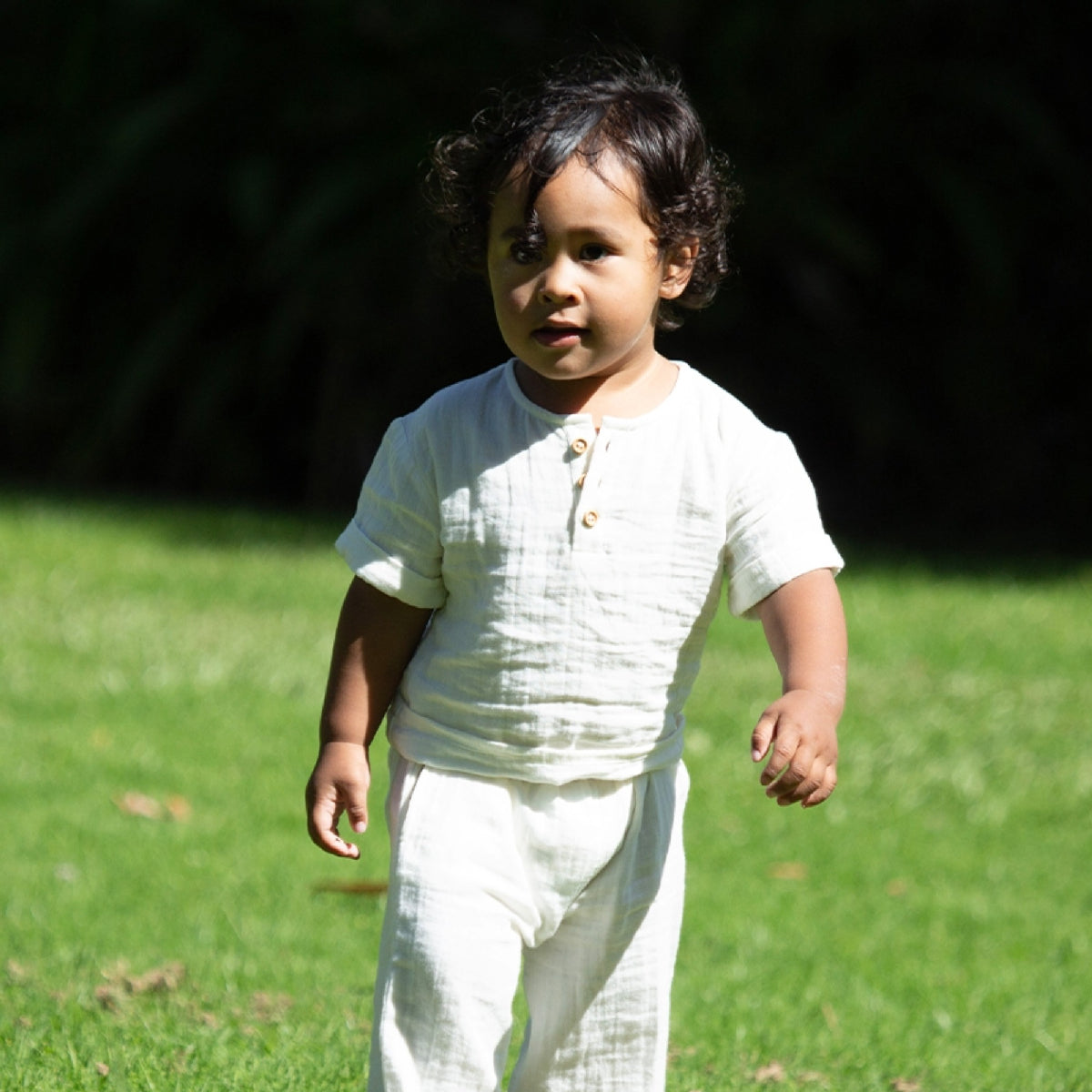 Child in a white outfit standing on grass with a blurred background