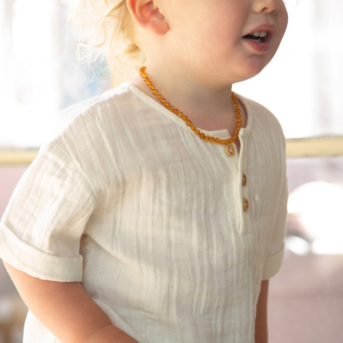 Child wearing a white shirt with buttons and an orange necklace indoors.
