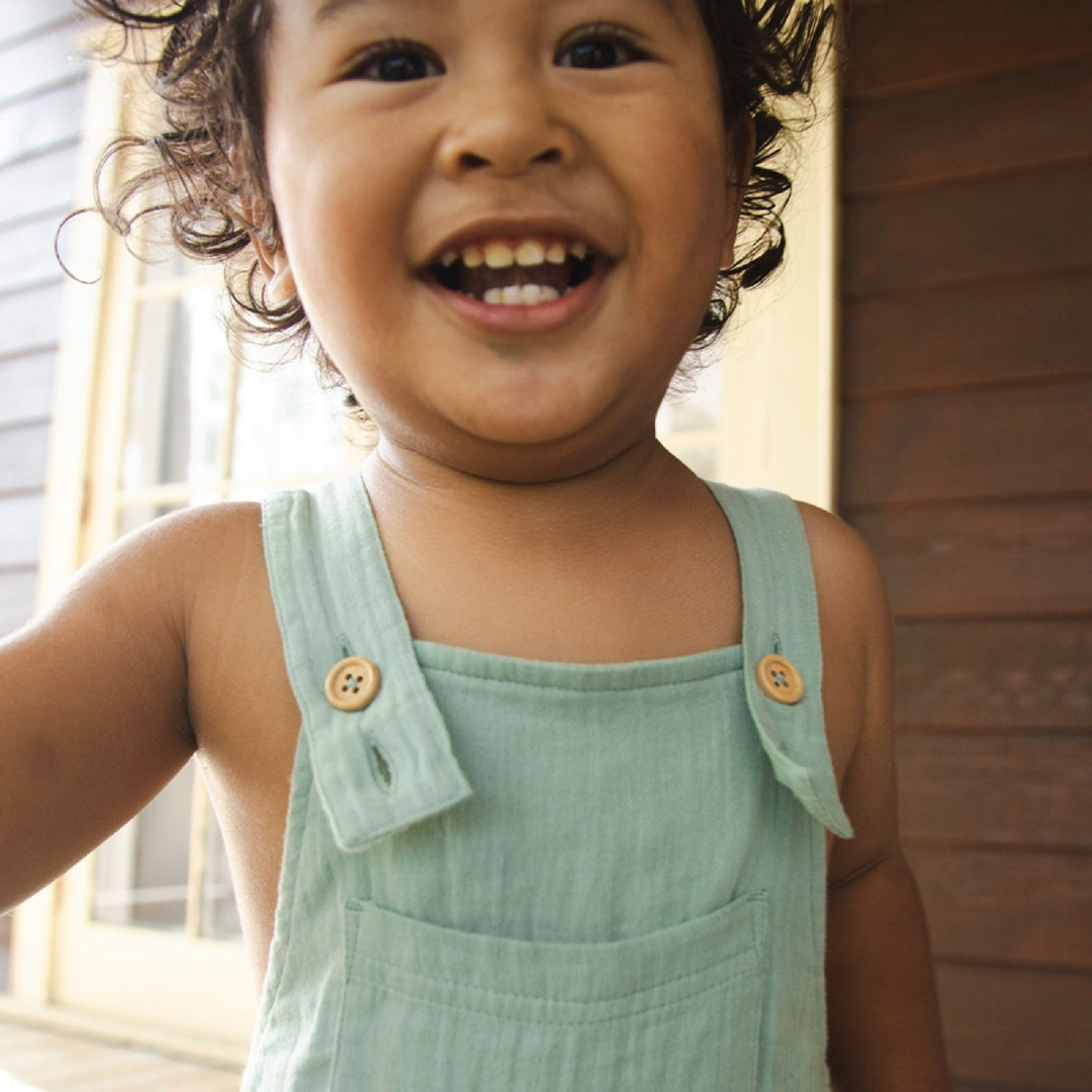 Child wearing a light green dress with buttons, standing outdoors.