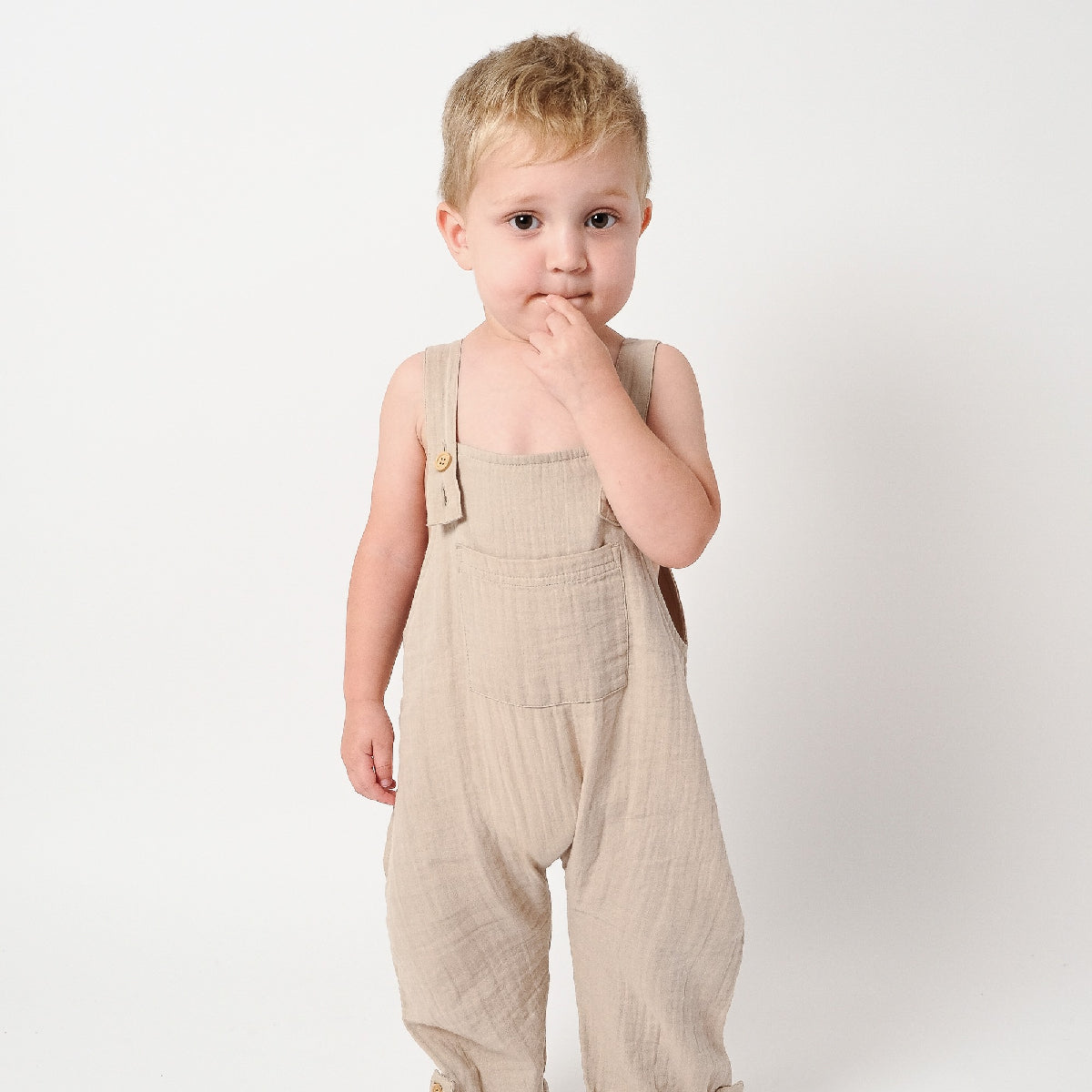 Child wearing beige overalls on a plain background