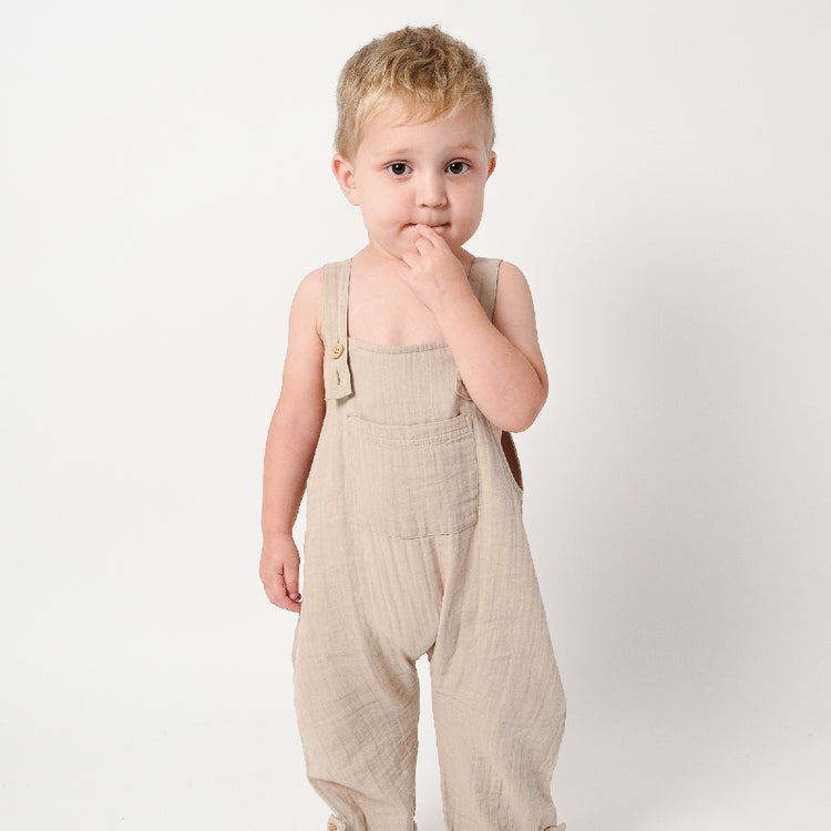 Child wearing beige overalls on a plain background