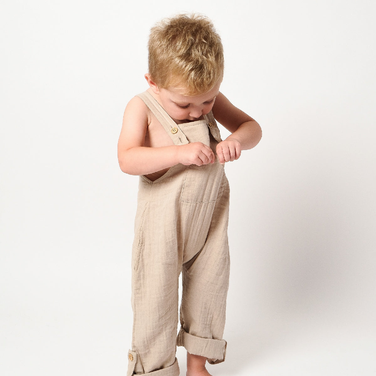 Child wearing beige overalls on a white background