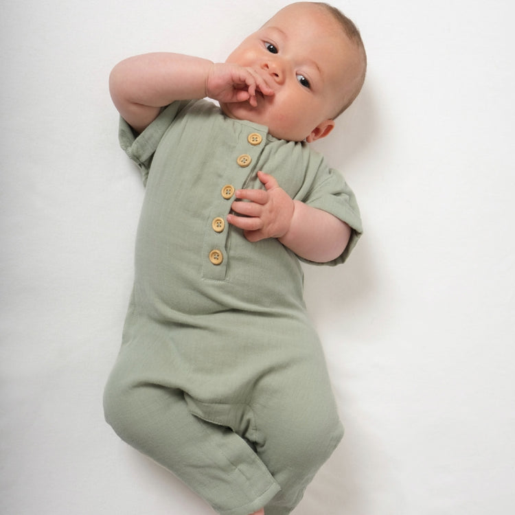 Baby wearing a green romper with button details on a white background