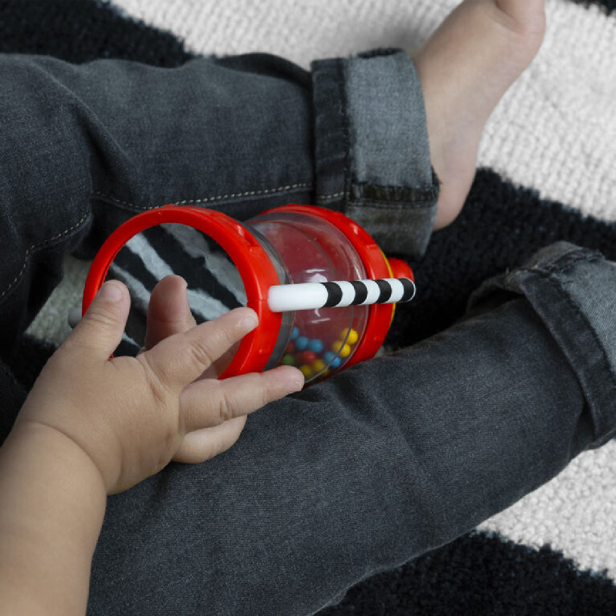 Child's hand holding a red cup with a straw on a striped fabric background