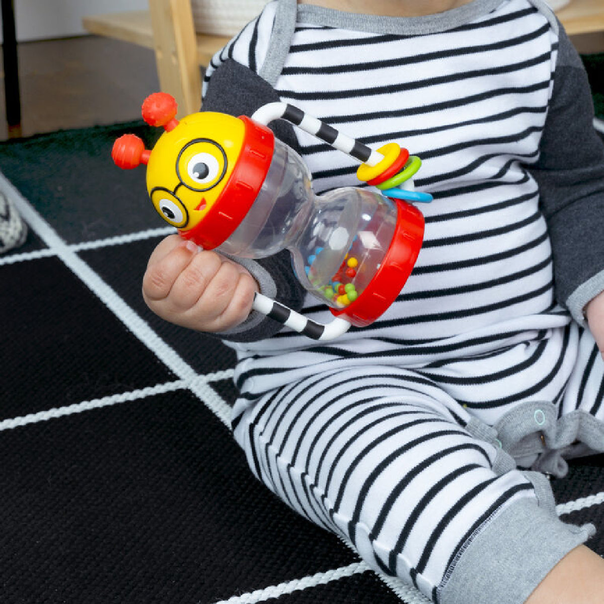 Child holding a colorful toy with a striped outfit on a checkered floor.