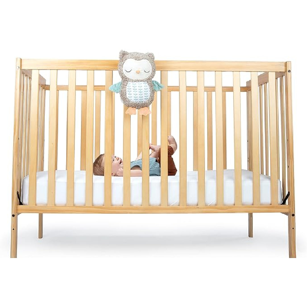 Wooden crib with a child inside and an owl-shaped toy hanging above on a white background