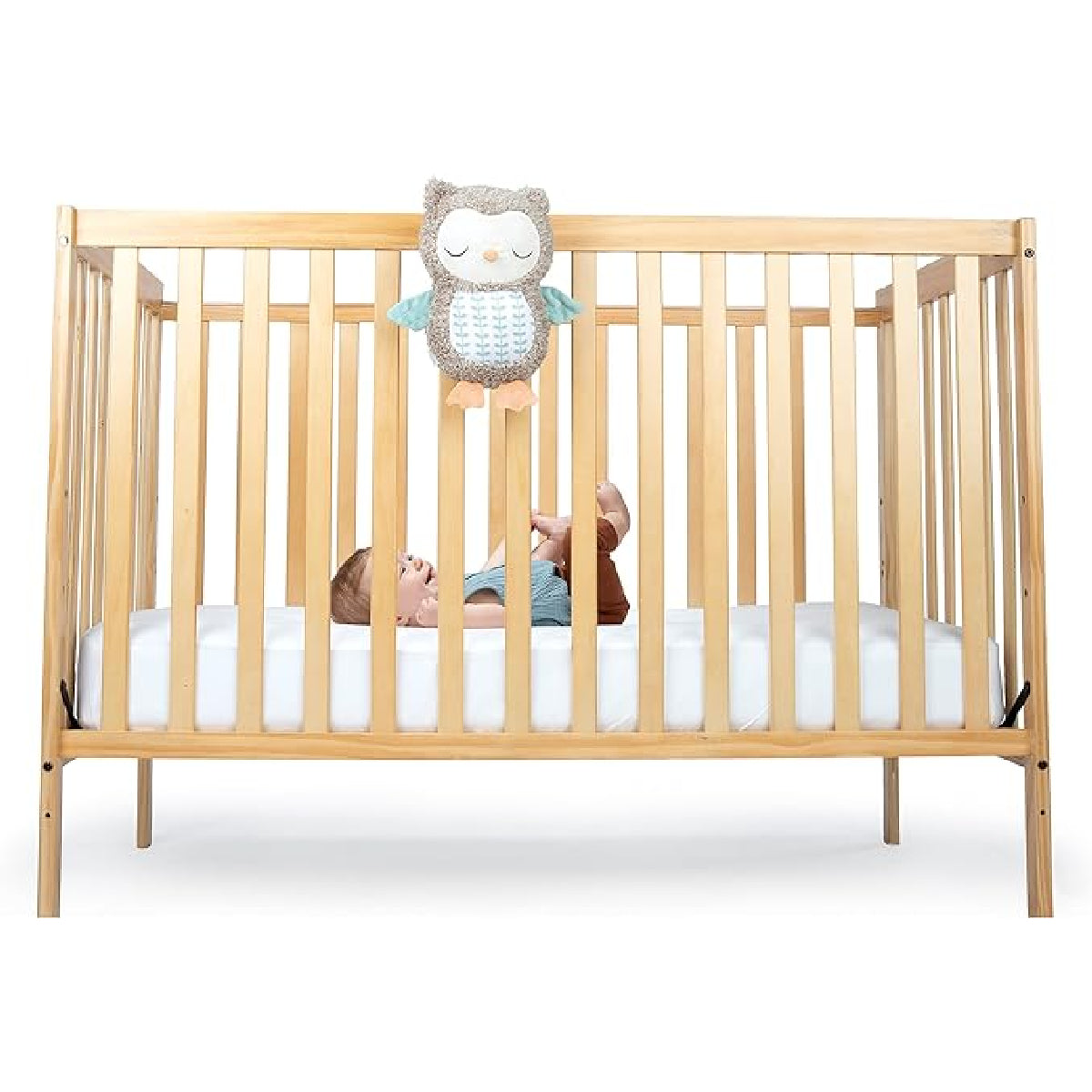 Wooden crib with a child inside and an owl-shaped toy hanging above on a white background
