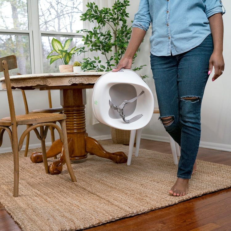 Person moving a white chair next to a wooden table in a room with plants and a window.