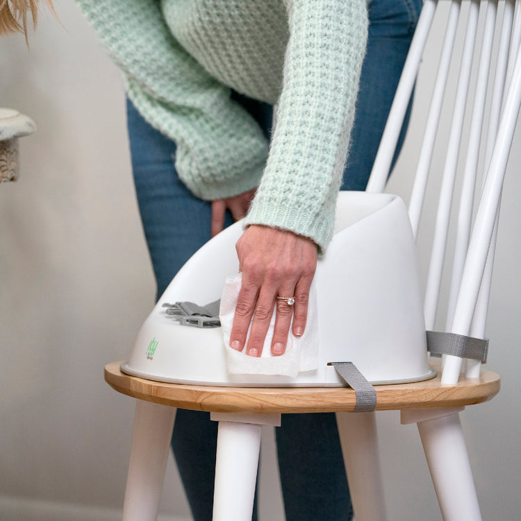 Person holding a white pet carrier on a wooden stool with a neutral background