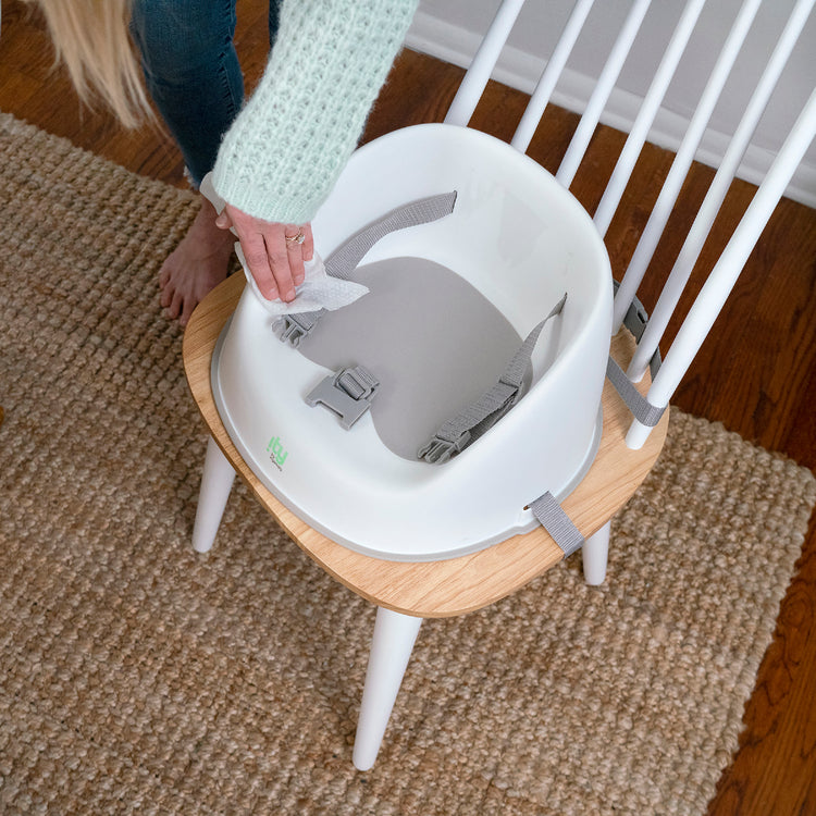 Baby high chair being adjusted on a wooden stool with a person's hand visible.