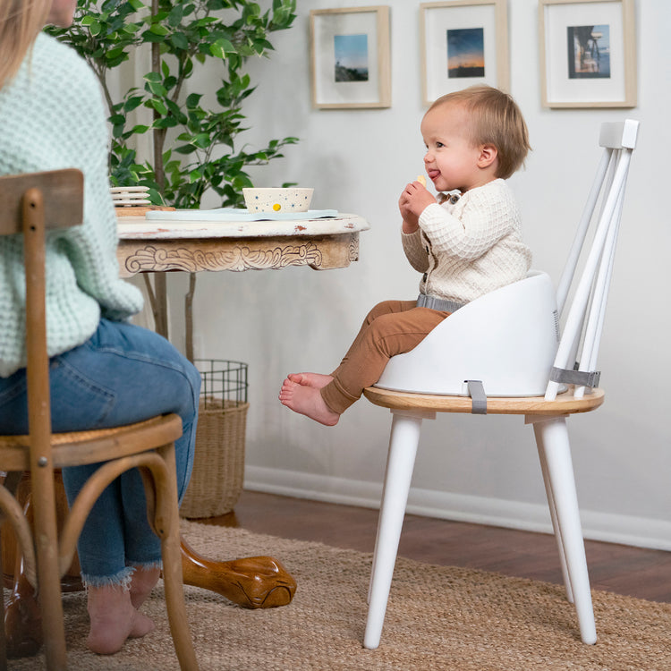 Child sitting in a high chair eating at a table with a person partially visible