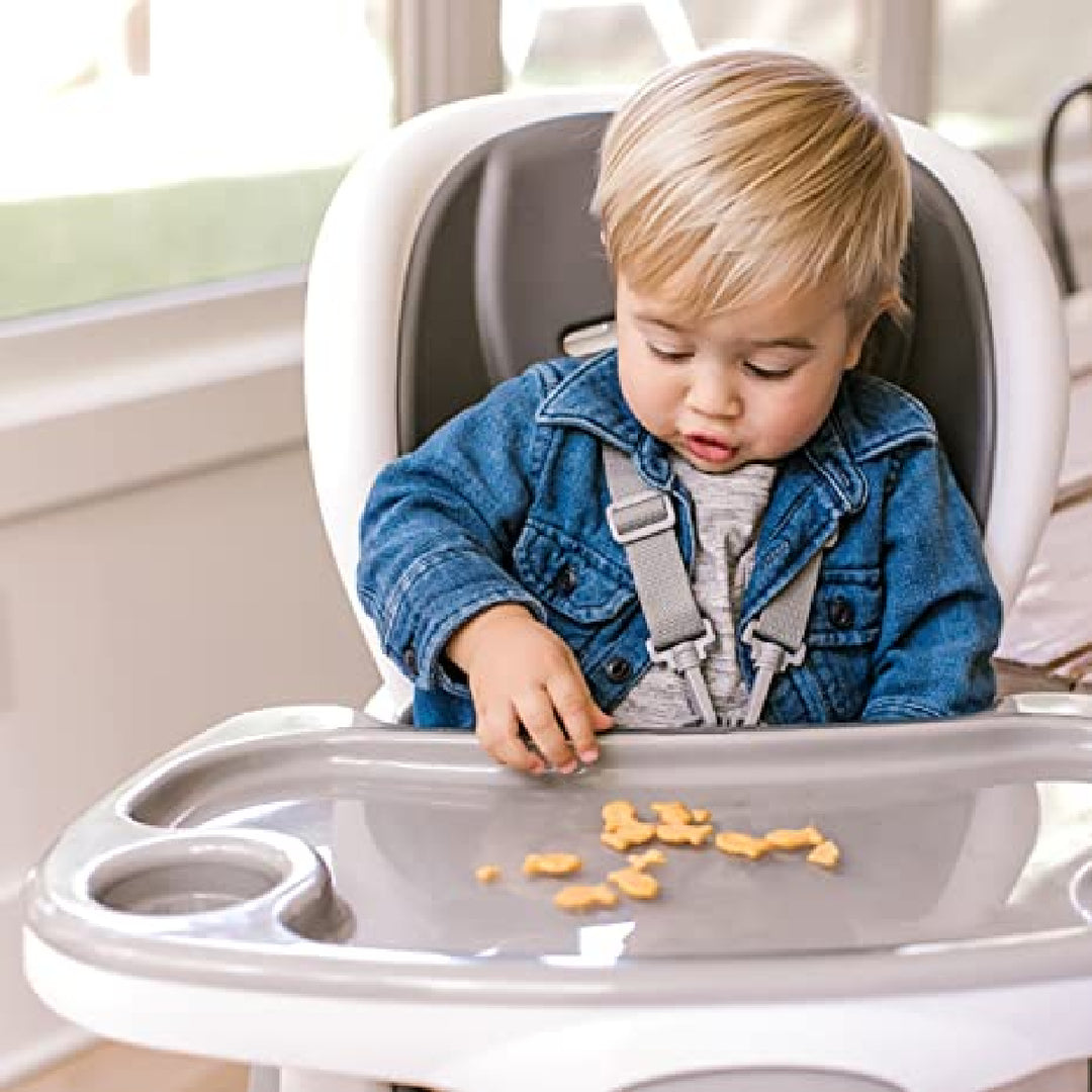 Child in a high chair with a tray, eating snacks indoors.