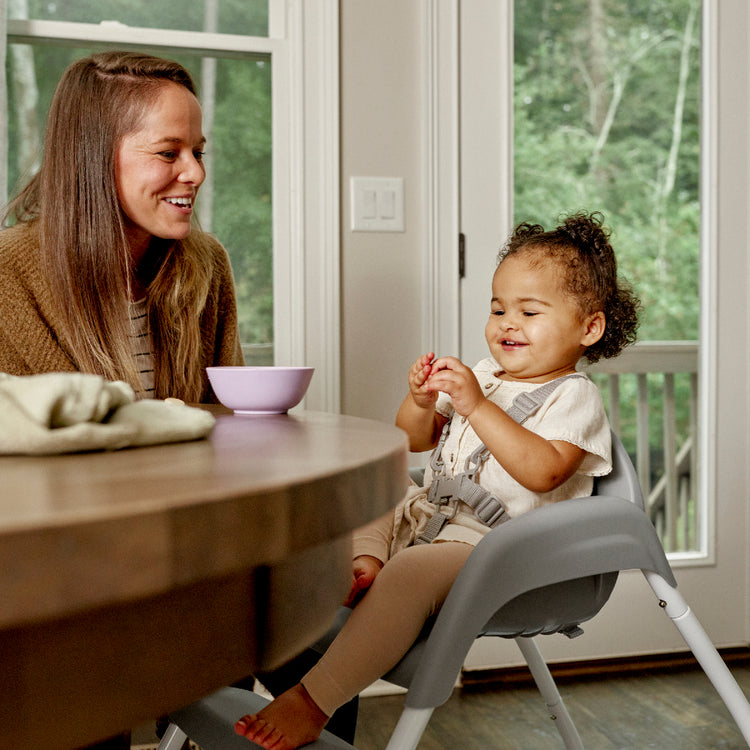Woman and child at a table with a bowl, smiling indoors.