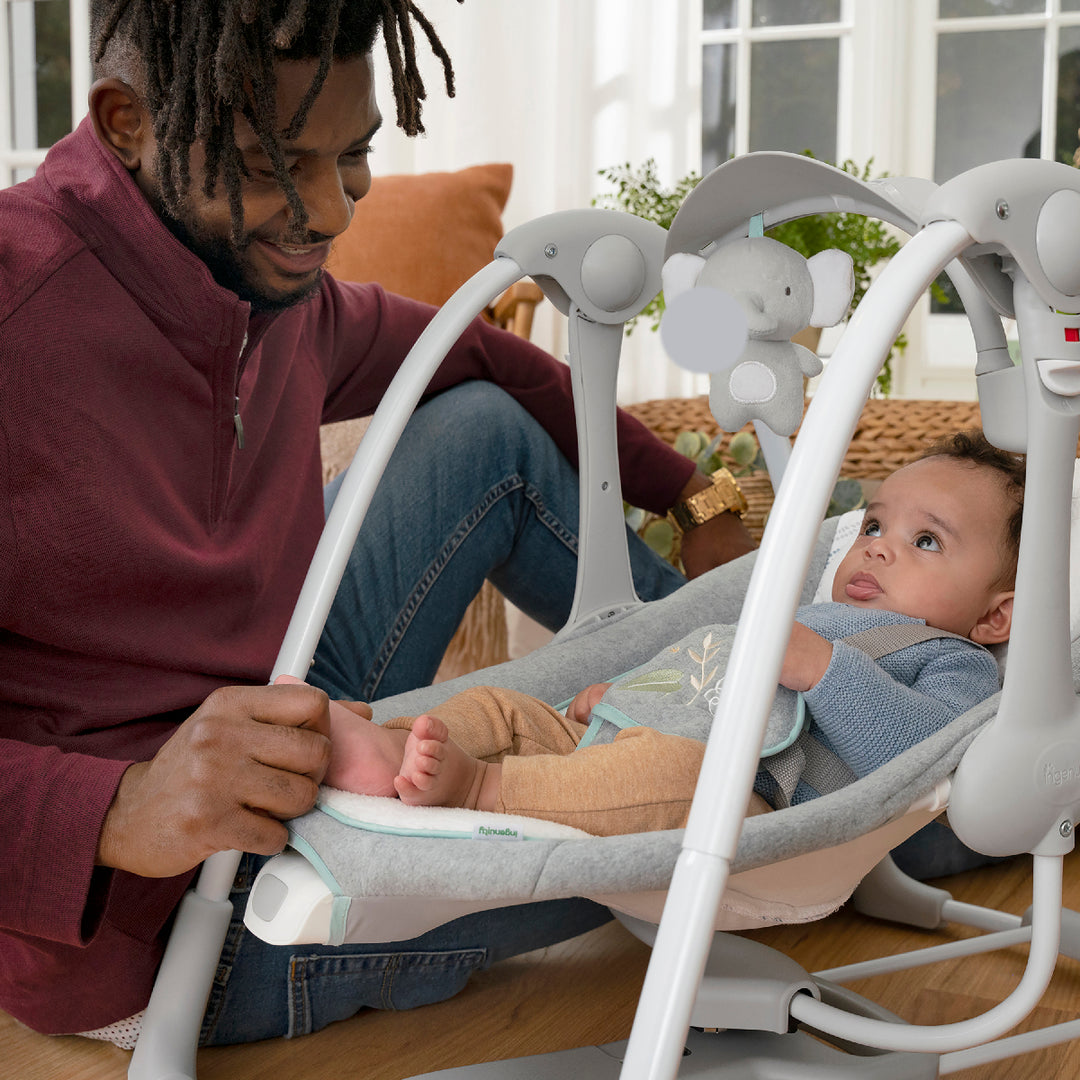 Man sitting with a baby in a white baby swing outdoors