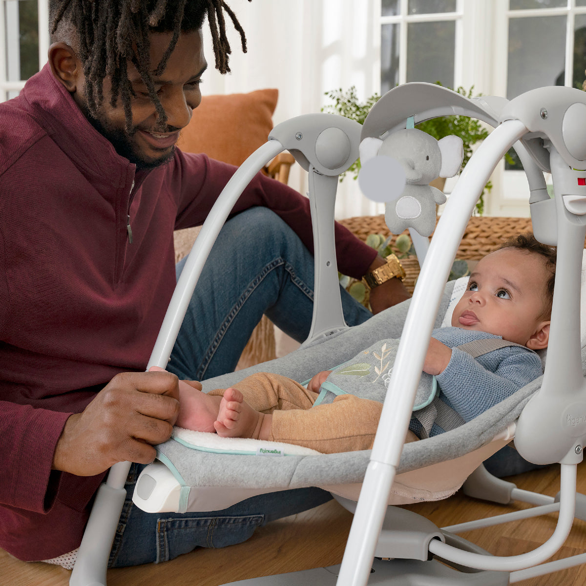 Man sitting with a baby in a white baby swing outdoors