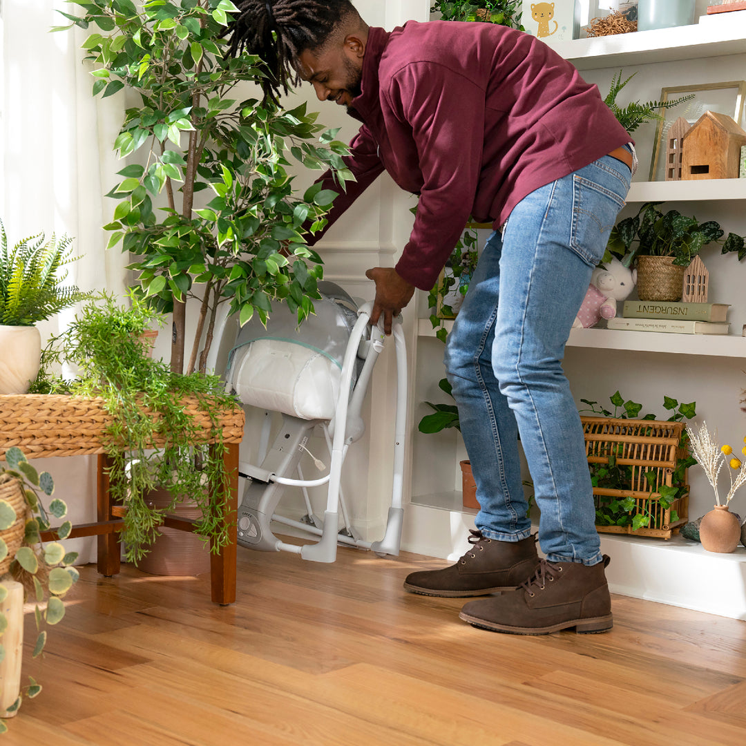 Person arranging plants in a home setting with wooden floors and white walls.