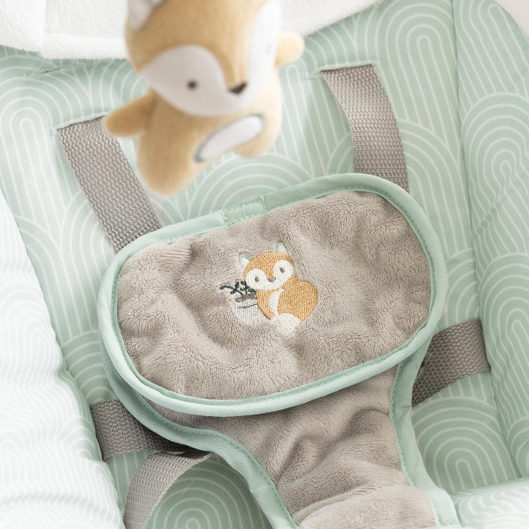 Baby bouncer with fox design and plush toy on a green and gray patterned surface