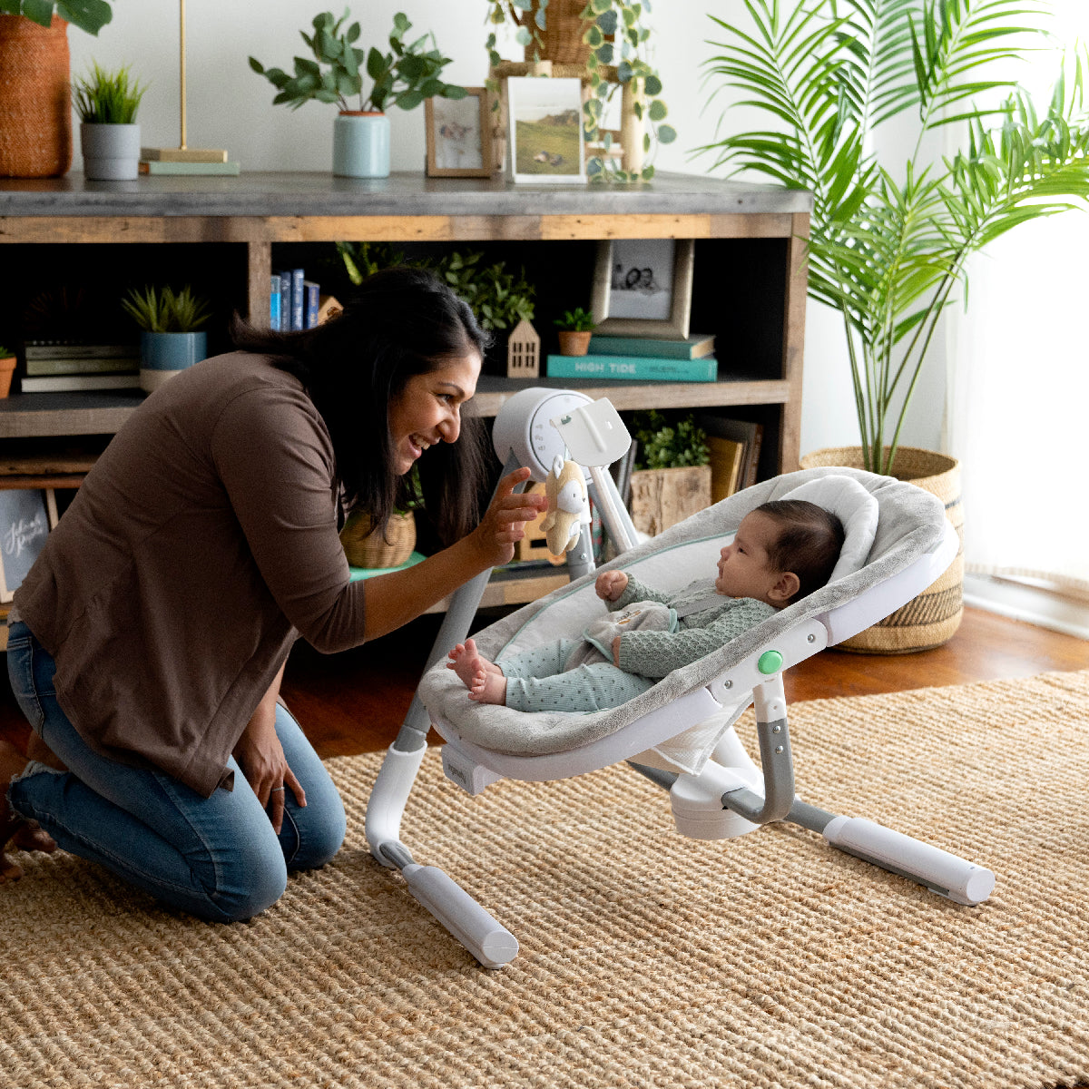 Woman interacting with a baby in a white baby bouncer in a home setting.