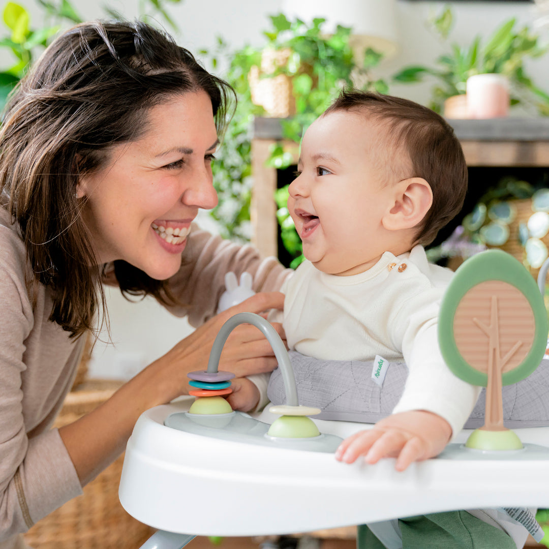 Woman and baby in a baby walker with toys, surrounded by greenery