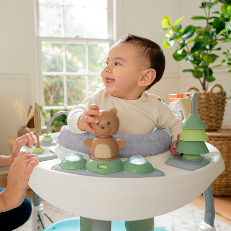 Baby in a high chair with toys, smiling in a home setting